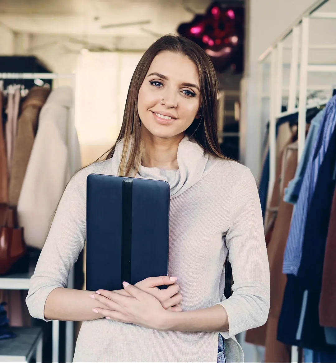 Boutique owner holding a folder among clothing racks in her shop