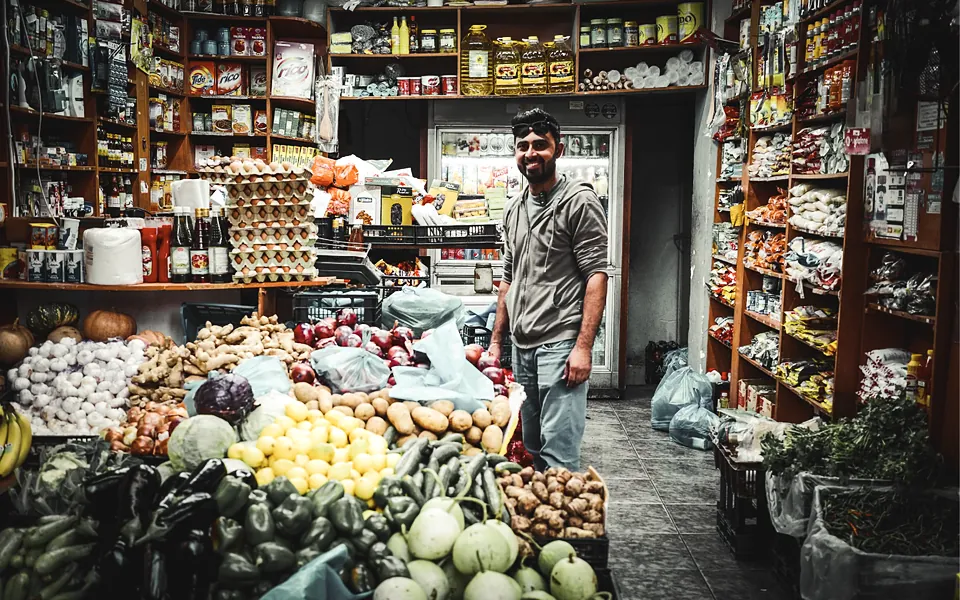 Grocer standing among fresh produce and stocked shelves in his store
