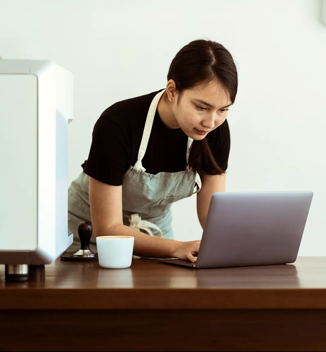 Café owner in an apron checking her laptop at the counter