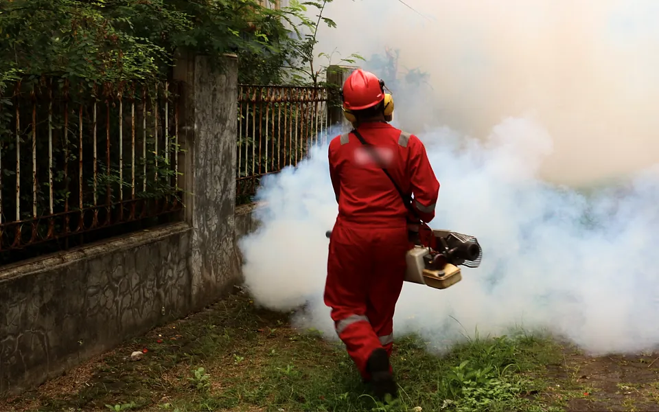 Pest control technician in protective gear fogging a yard