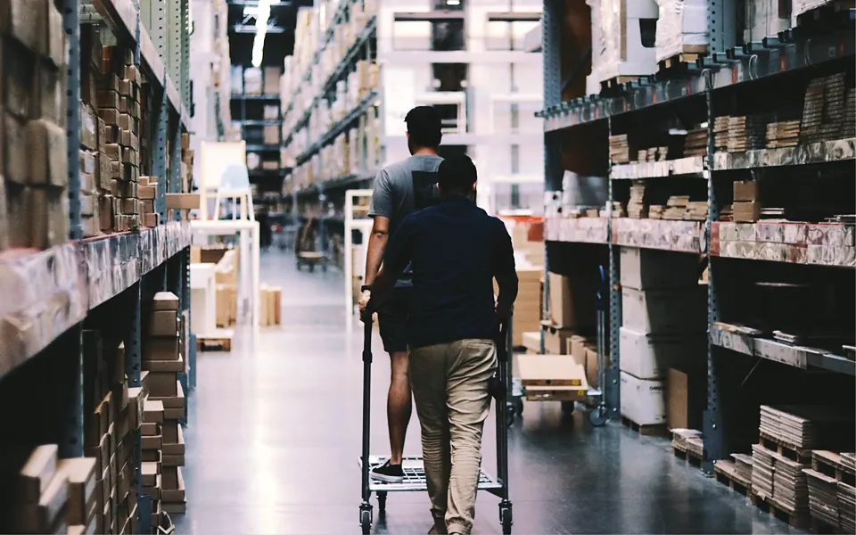 Two workers pushing a cart down a stocked warehouse aisle