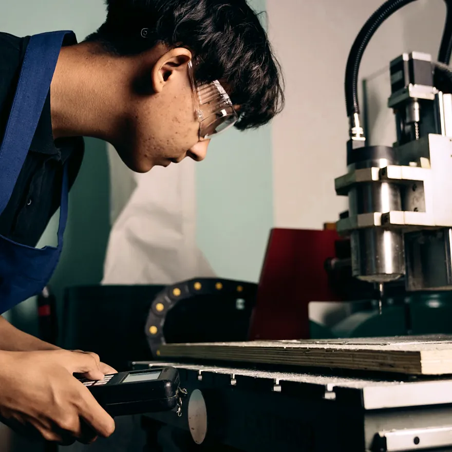 Machinist operating a CNC router with a handheld controller in a workshop