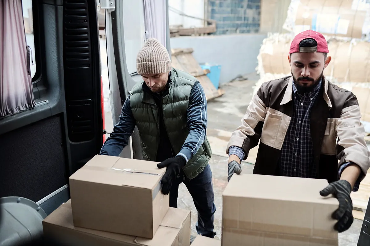 Two workers loading boxed customer orders into a delivery van